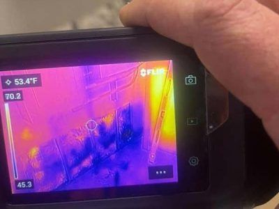 Thermal camera displaying heat signature of an object, held by a hand. Colors range from purple to yellow, indicating varying temperatures.