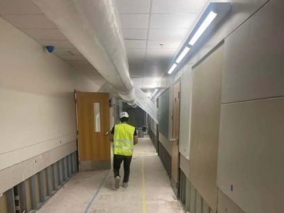 A construction worker walks down a hallway with exposed walls and ceiling ductwork.