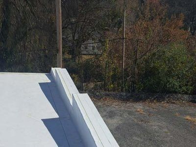 White roof edge with stacked blocks, overlooking trees and asphalt.