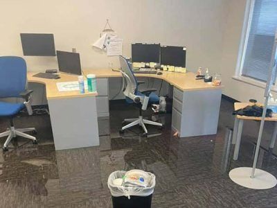 Office with water on the floor, desks with monitors, chairs, and trash bin.
