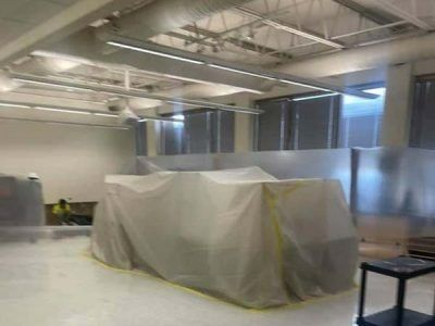Interior construction site with covered equipment, ductwork, and a worker.