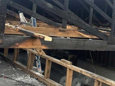 Charred wooden roof structure with exposed beams, ladder, and debris.