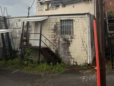 Weathered, one-story building with door, stairs, window. Metal ladder on the side. Overcast sky.