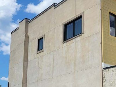 Tan stucco building with black-framed windows against a blue sky.