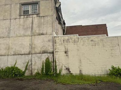 Weathered building exterior with overgrown weeds and cracked walls.