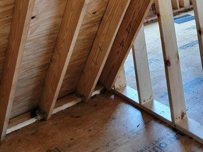 Wooden rafters and framing in an unfinished construction, angled against plywood walls and flooring.
