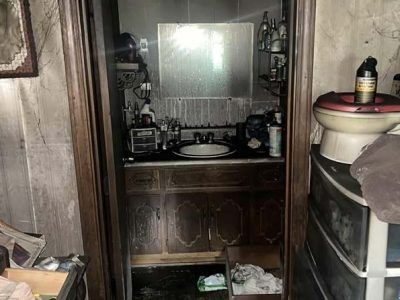 Dirty, cluttered bathroom with dark wood cabinets, a mirror, and a toilet.