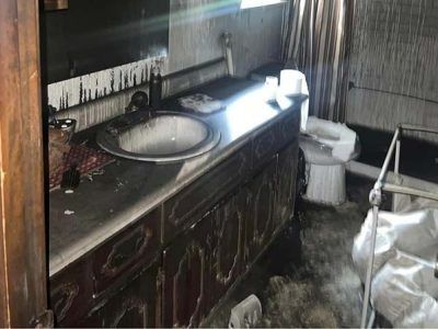Bathroom interior heavily damaged by fire: soot-covered sink, vanity, toilet, and walls.