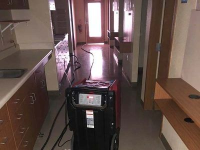 Dehumidifier in a hallway with bright light at the end, likely for water damage remediation.