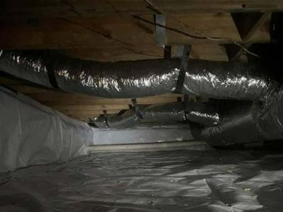 Crawl space with ductwork and insulation, with vapor barrier on the ground.