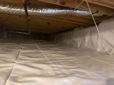 Crawl space with white vapor barrier covering the floor and walls, wooden beams overhead.