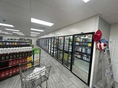 Interior view of a convenience store with refrigerated drink cases, products on shelves, and a shopping cart.