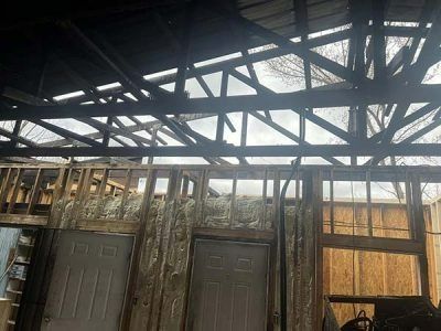 Partially dismantled barn interior; exposed beams, insulation, two doorways, and weathered wooden walls. Cloudy sky visible.