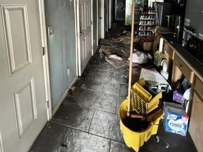 A damaged hallway with debris and cleaning supplies; likely fire or water damage.