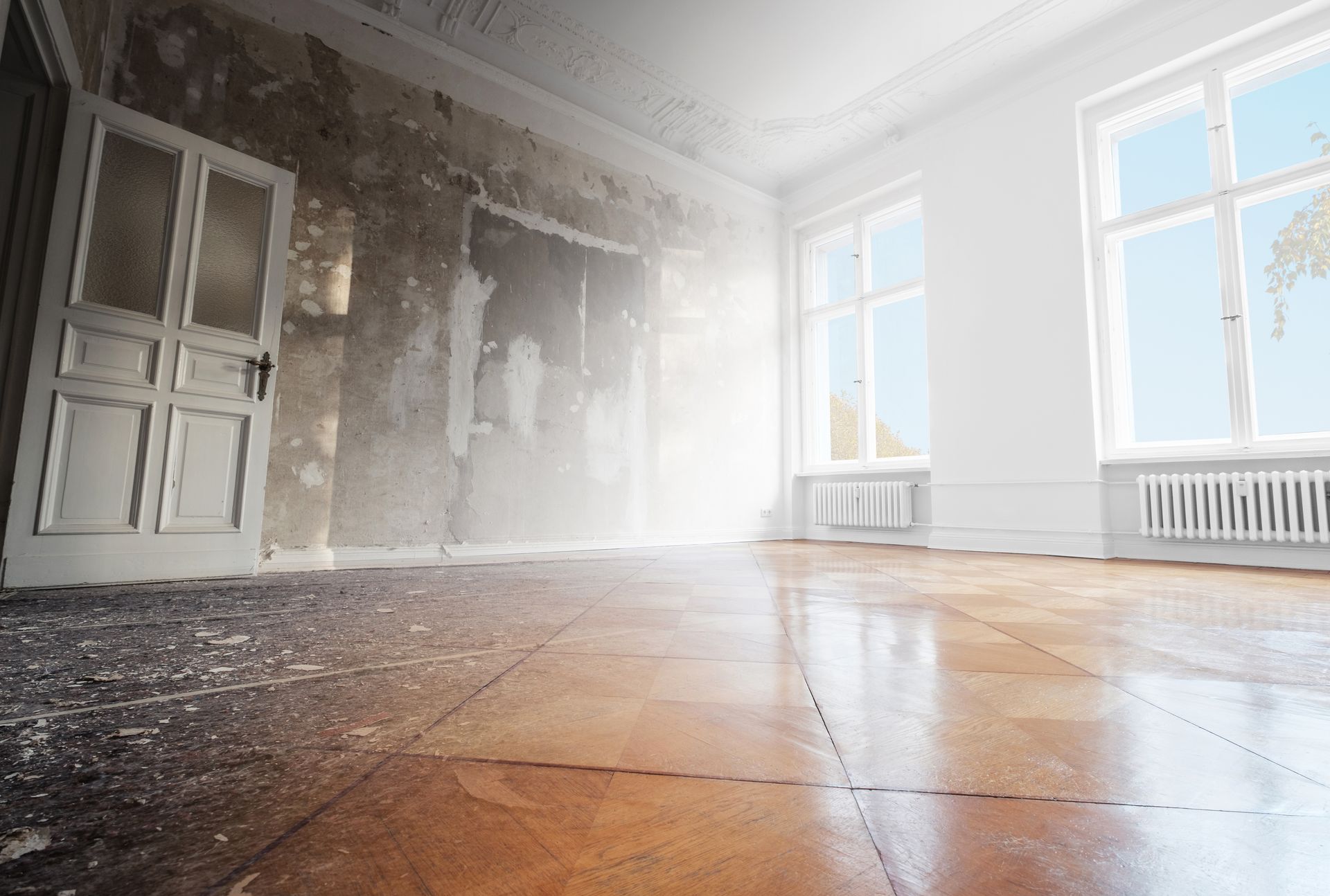 Empty, sunlit room with bare walls, large windows, and worn wooden floorboards