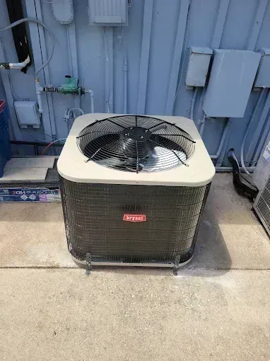 An outdoor air conditioning unit with a fan and coils, against a light blue wall.