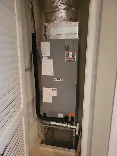 HVAC unit in a closet. The gray unit has labels, black vent tubing, and white PVC pipes on a metal stand.