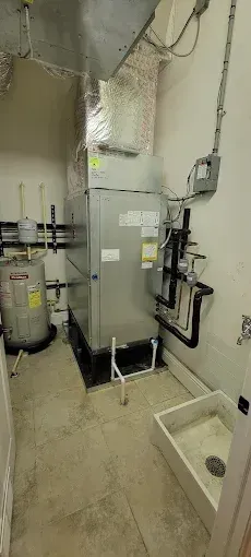 HVAC unit in a utility room next to a water heater and utility sink.