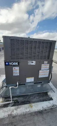 A YORK rooftop air conditioning unit on a white concrete surface, against a cloudy blue sky.
