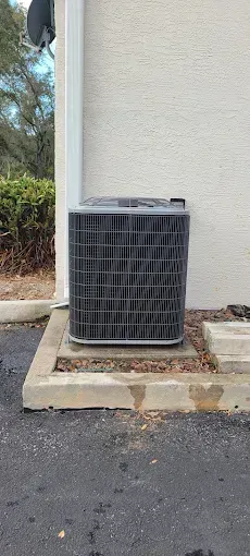 Air conditioner unit on a concrete pad next to a beige building.