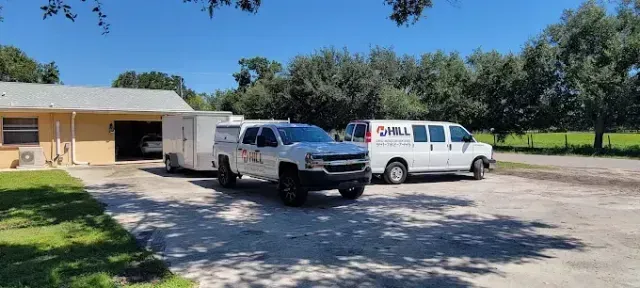 A light-colored pickup truck pulling a trailer next to a white van parked in front of a building.