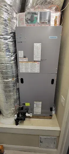 A gray HVAC unit in a room with a white base. Ductwork and access door are visible.