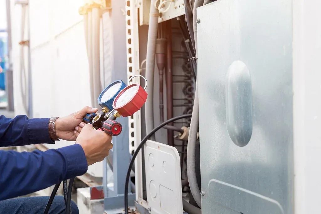 HVAC technician using gauges to service an air conditioning unit outdoors.