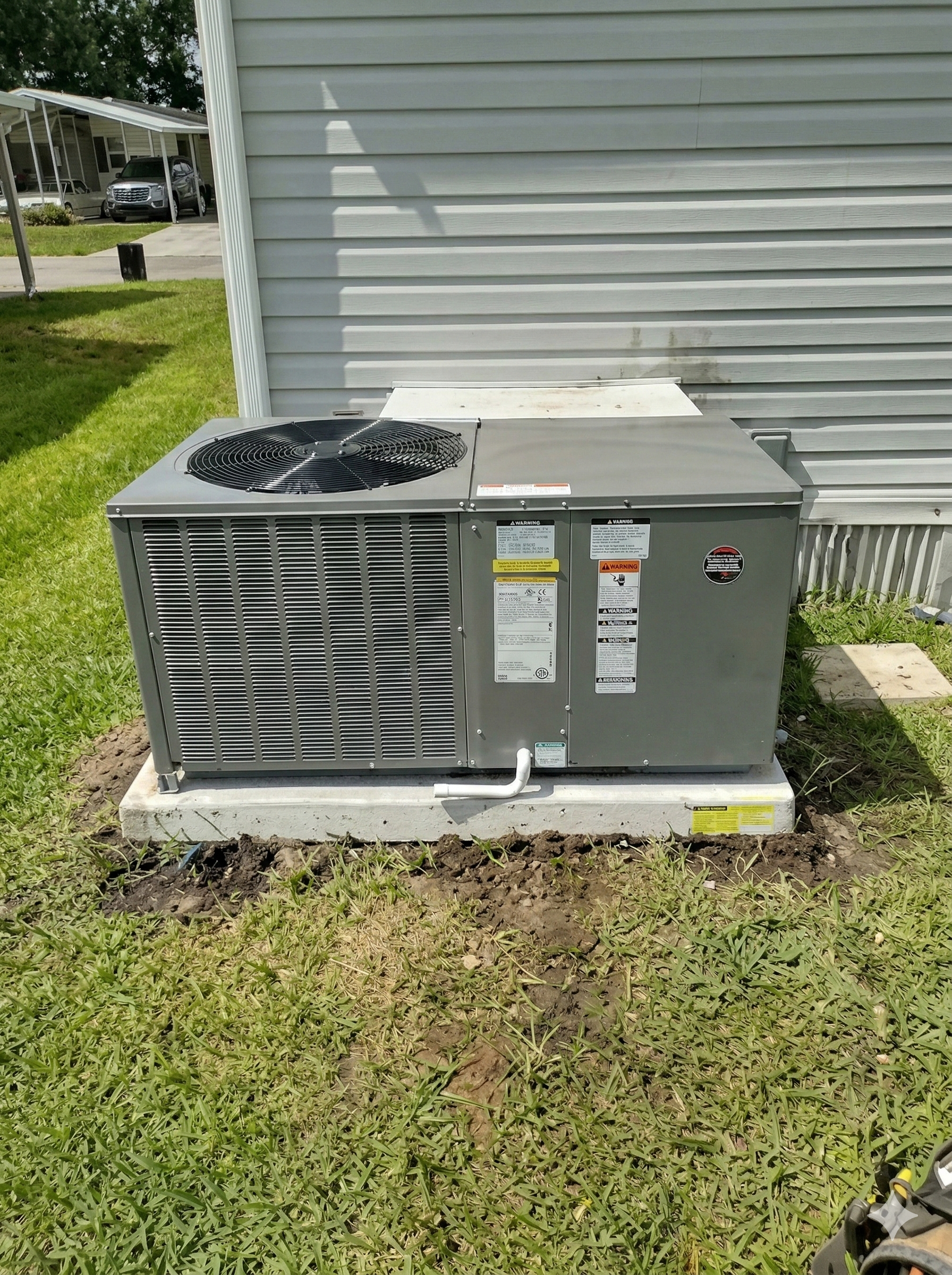 Gray air conditioning unit on a concrete pad next to a light gray house with green grass.