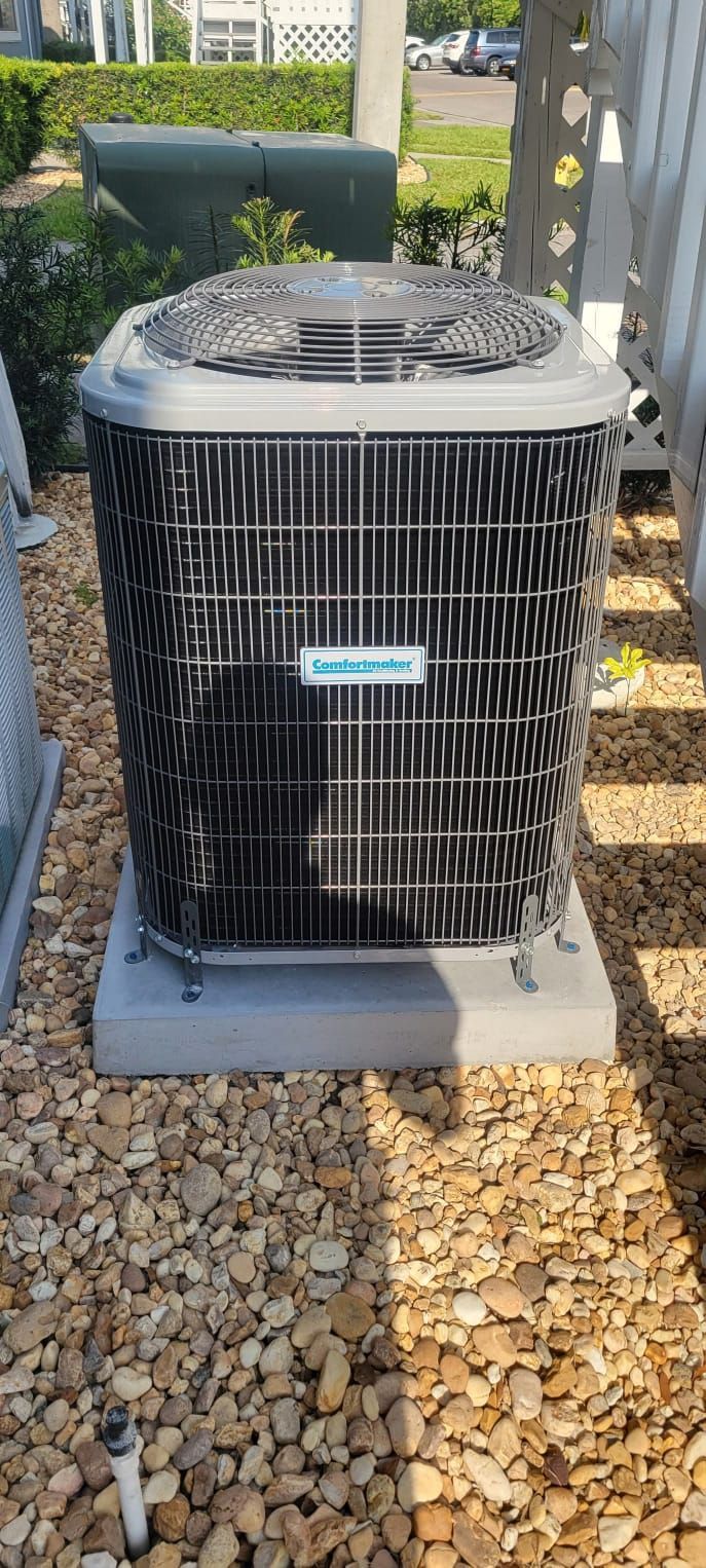 Air conditioning unit on a concrete base, set on a bed of small pebbles.