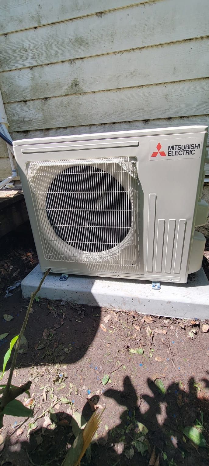 Mitsubishi Electric air conditioner unit outside against a white wooden wall, on a concrete base.