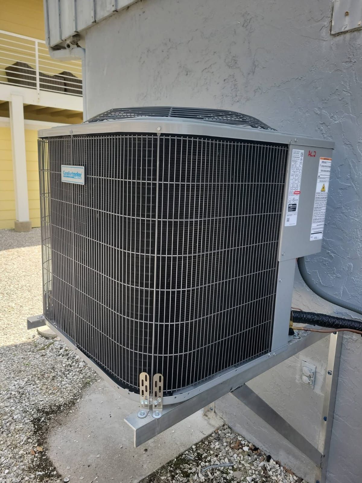 Gray air conditioning unit mounted on a concrete wall outside a building.