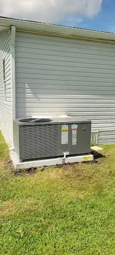 An air conditioning unit on a concrete pad next to a light gray house with green grass.