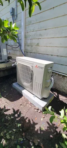 Mitsubishi air conditioning unit on a concrete block next to a building wall.
