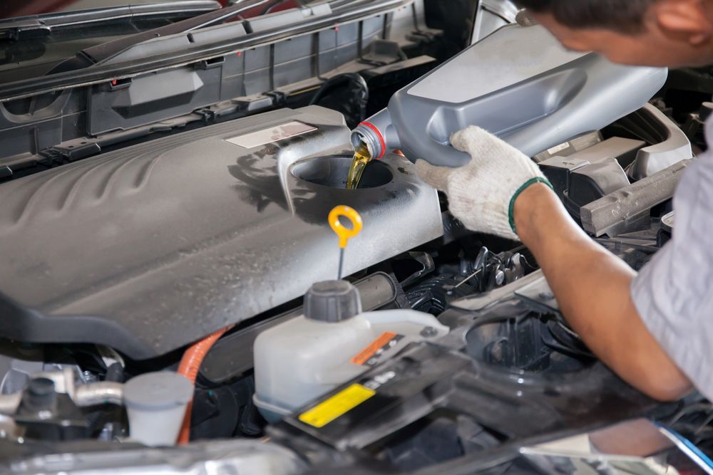 A Man is Pouring Oil Into a Car Engine — J & W Mechanical In Elermore Vale, NSW
