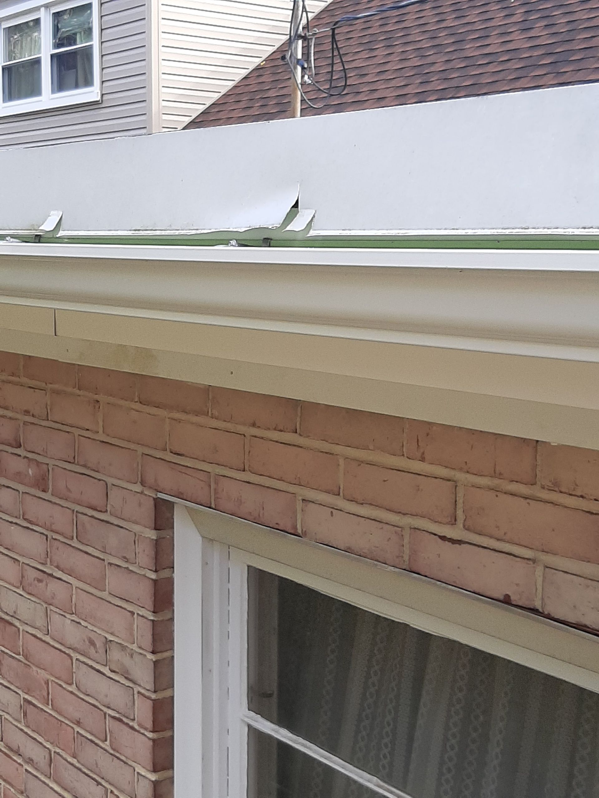 Brick building with beige trim, white window and roof with metal flashing.