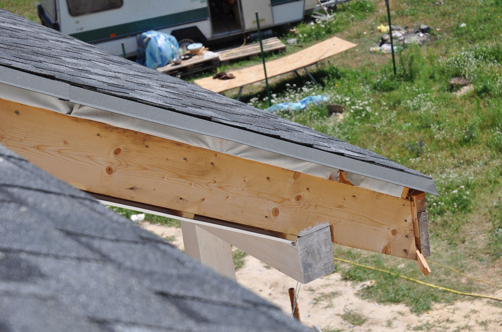 Wooden roof overhang with gray shingles and metal flashing.