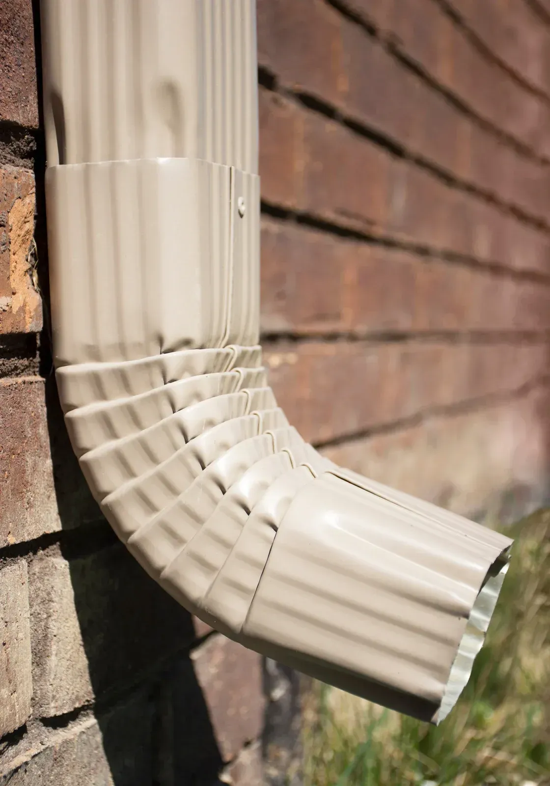 Beige gutter downspout attached to a brick wall.