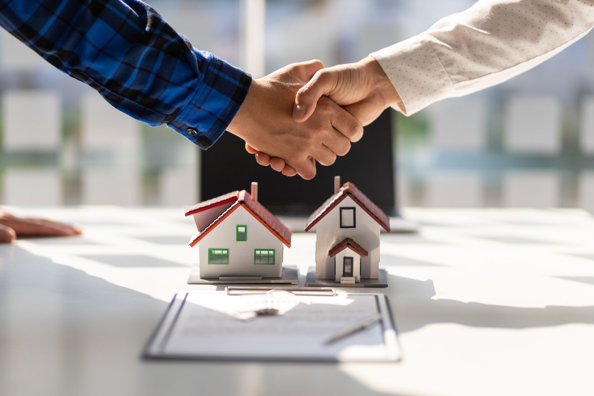 A man and a woman are shaking hands over a table with two small houses.
