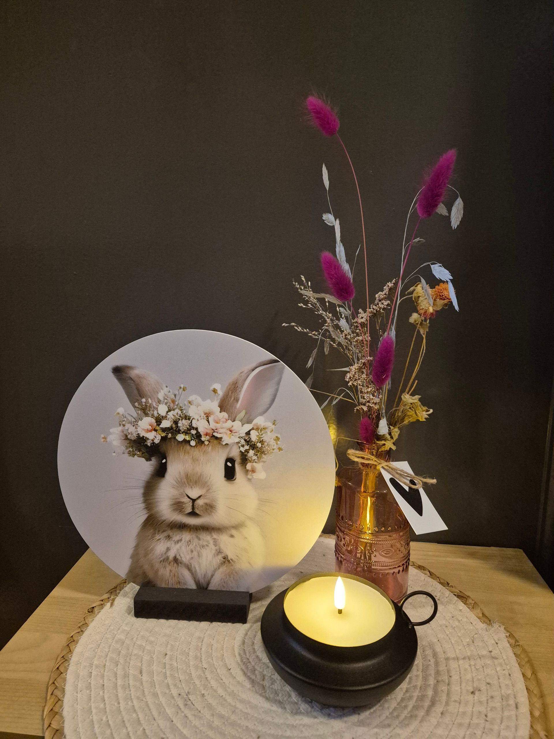 Paashaasdecoratie met kaars en gedroogde bloemen op een tafel.