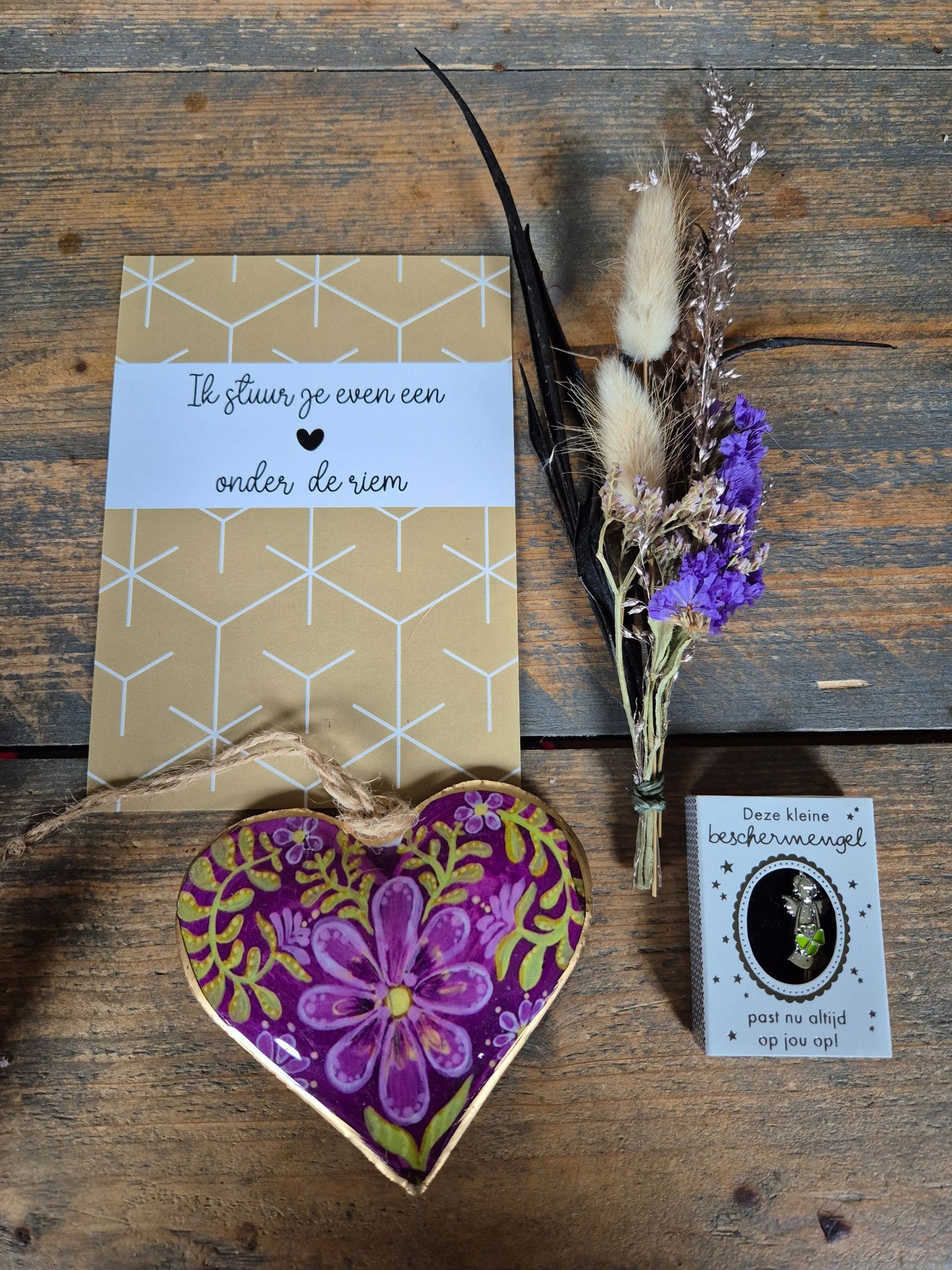 Cadeauverpakking met een hartvormig bloemenornament, gedroogde bloemen en kaartjes. Roze, goud en paarse kleuren.