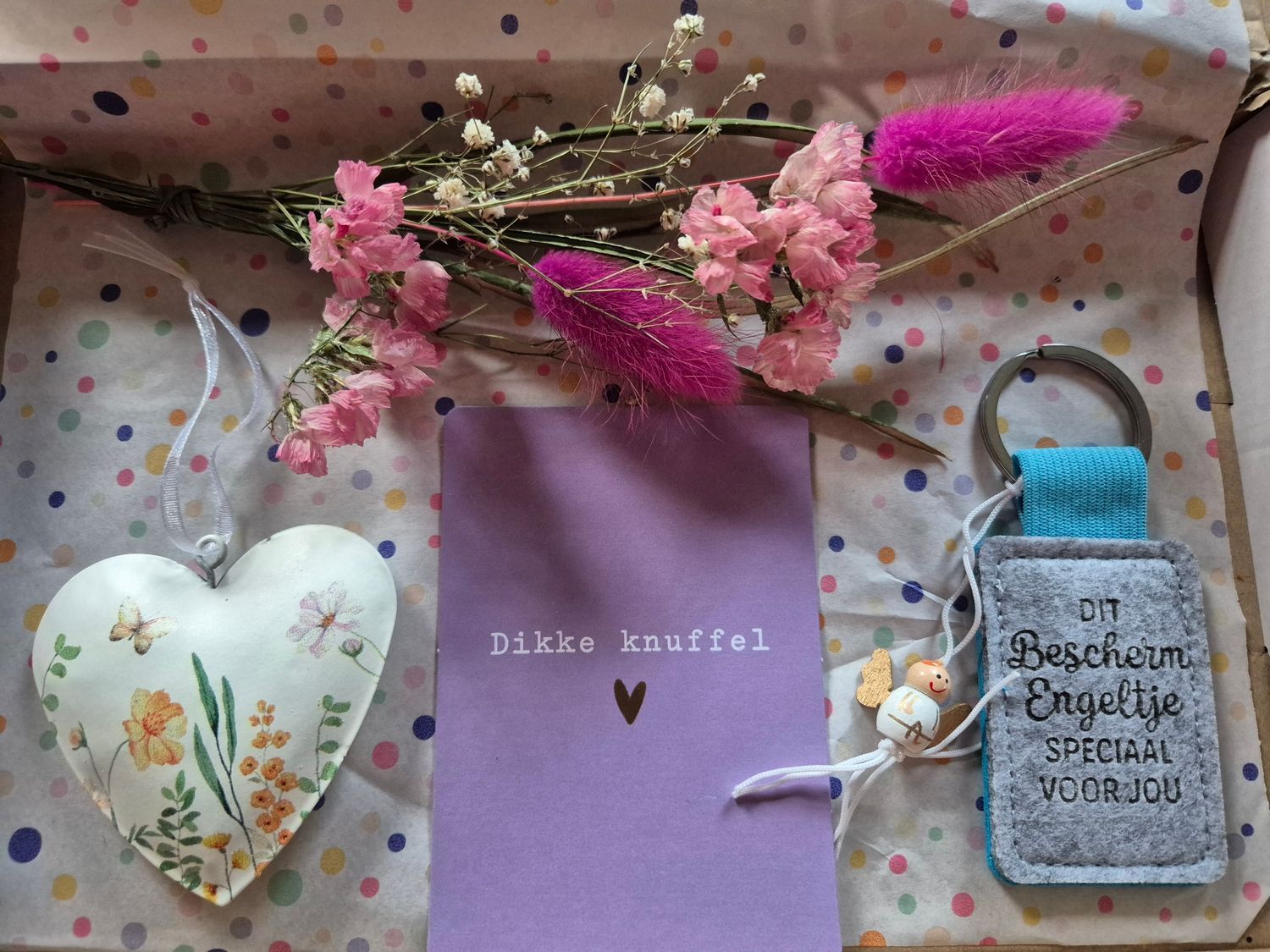Doos met gedroogde bloemen, een hartvormig ornament, een paarse kaart met een hartje en een sleutelhangertje.