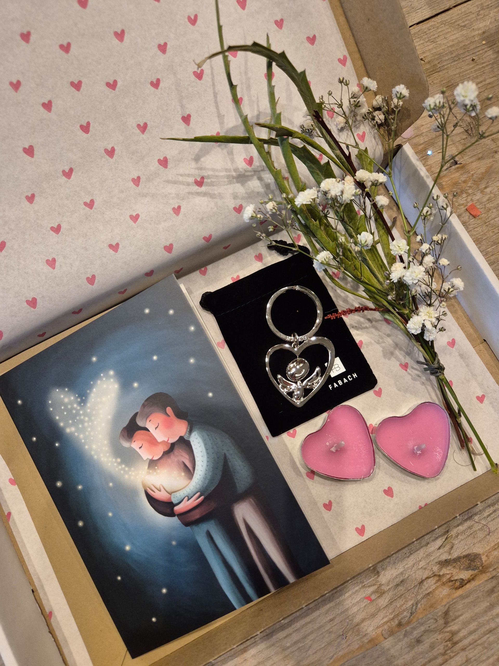 Cadeauverpakking met een kaartje, sleutelhangertje, hartvormige kaarsen en bloemen. Op het kaartje staan ​​twee mensen die elkaar omarmen met een stralend hart.
