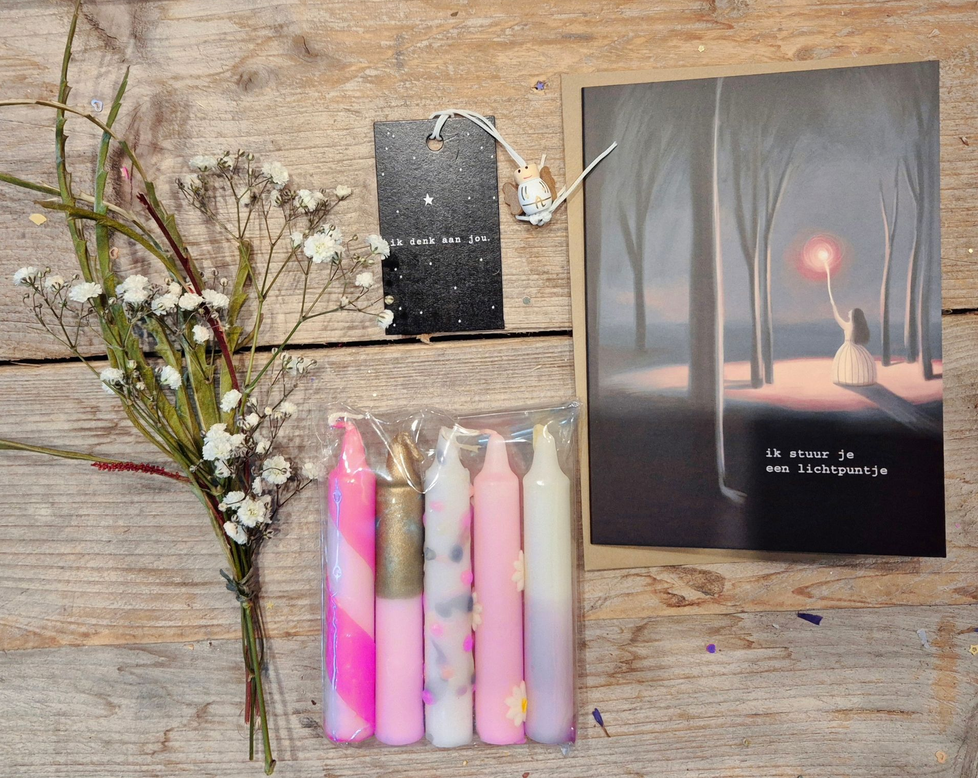 Een geschenkdoos met kaarsen, bloemen en een kaart met een schilderij erop. Roze en witte tinten.