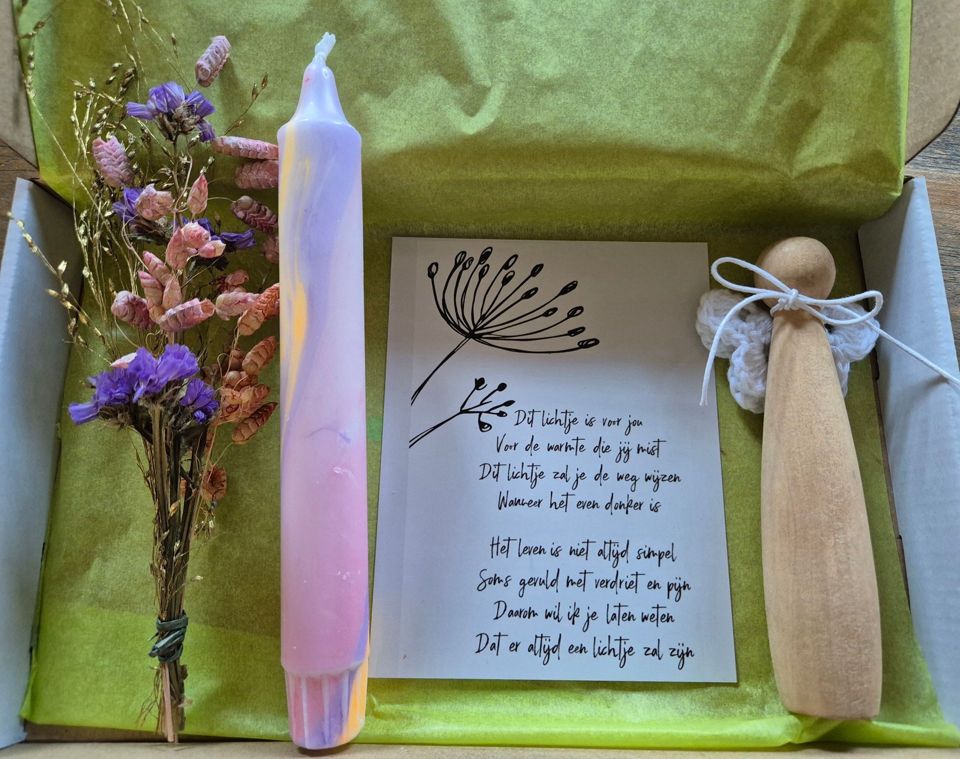 Kaart met tekening en tekst, paarse kaars, gedroogde bloemen en houten engel op een houten ondergrond.