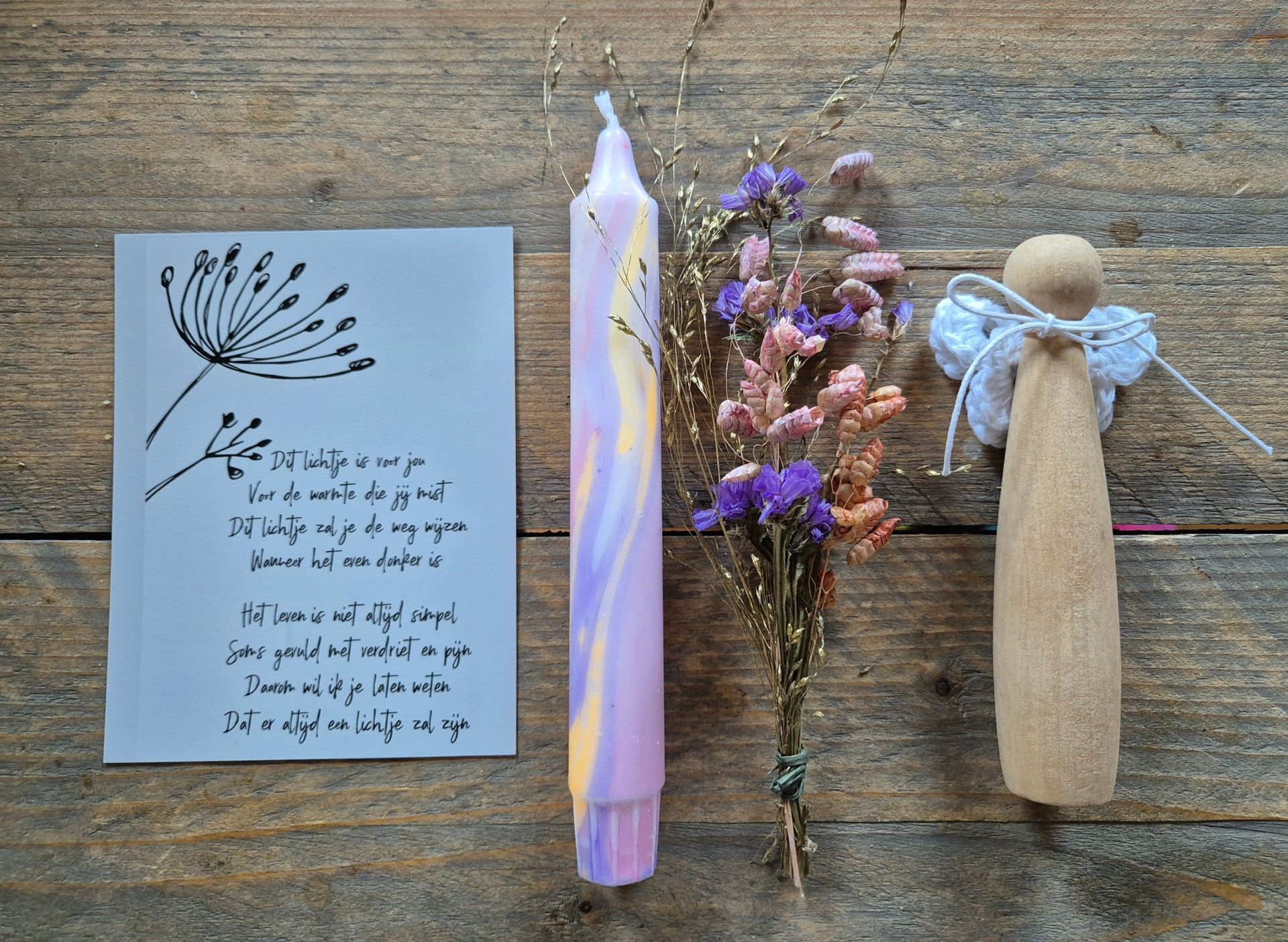 Kaart met tekening en tekst, paarse kaars, gedroogde bloemen en houten engel op een houten ondergrond.
