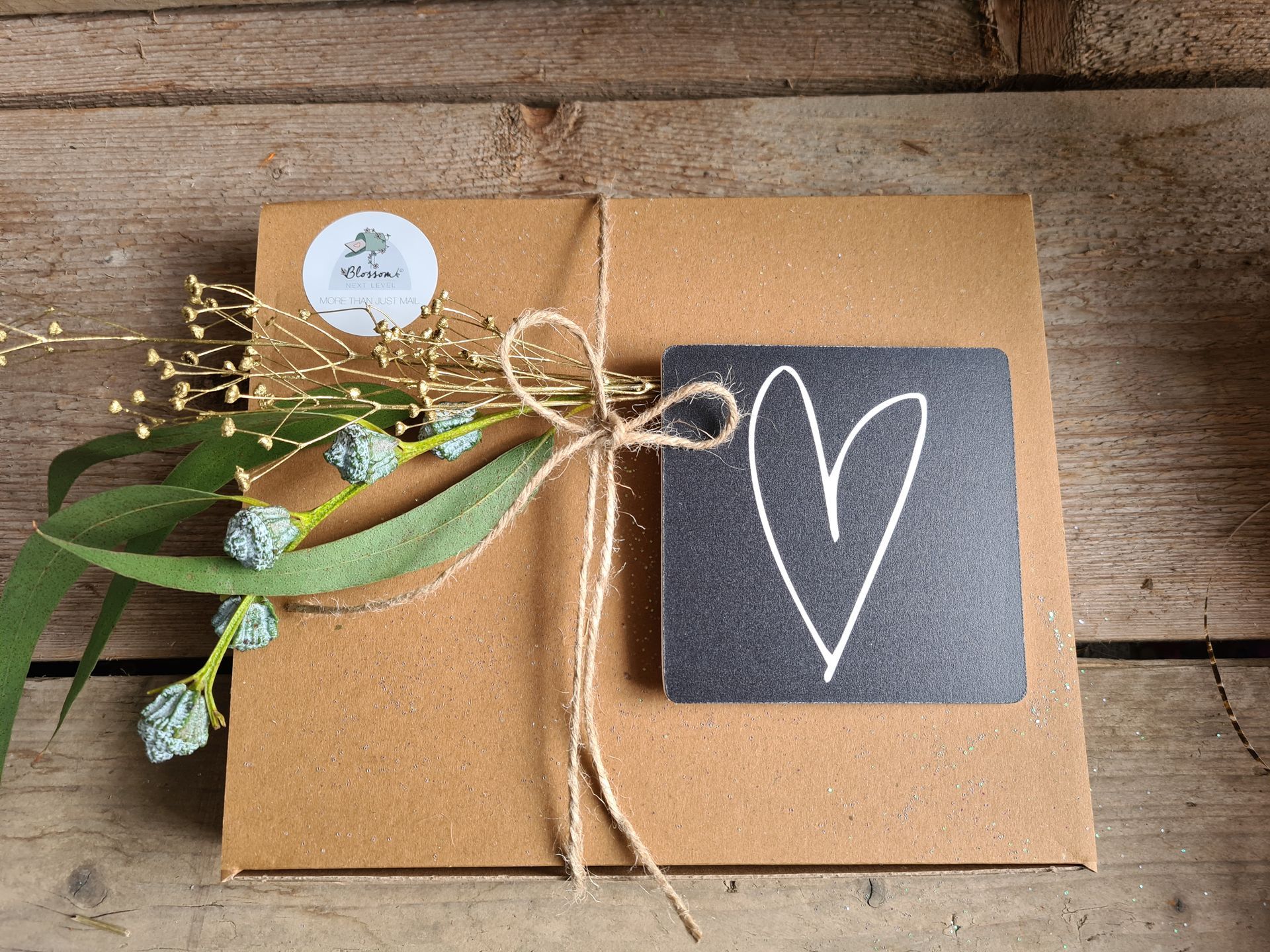Een bruine geschenkdoos, vastgebonden met touw, versierd met groen en een krijtbordlabel met een getekend wit hartje.