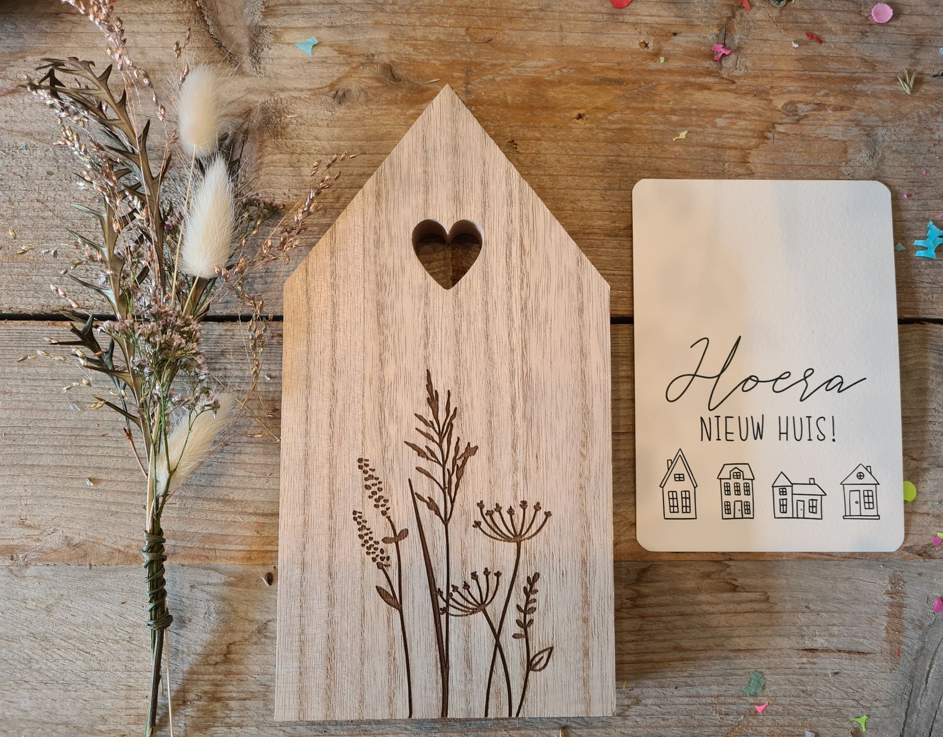 Houten huisvormige decoratie met gegraveerd bloemmotief en hartvormige uitsparing, met een kaartje waarop 