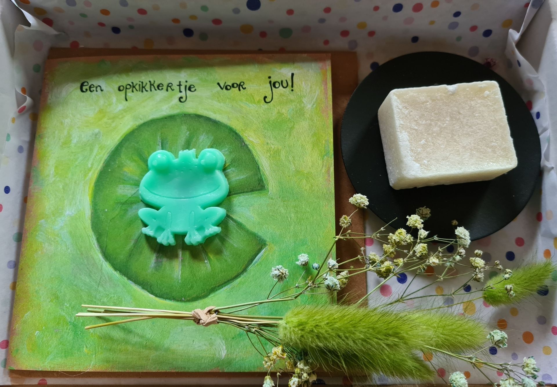 Wenskaart met een kikker, zeep en bloemen op een houten achtergrond.