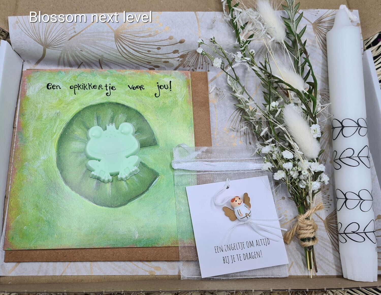 Doos met een wenskaart, een kaars en bloemen. Op de kaart staat een kikker op een waterlelie afgebeeld.