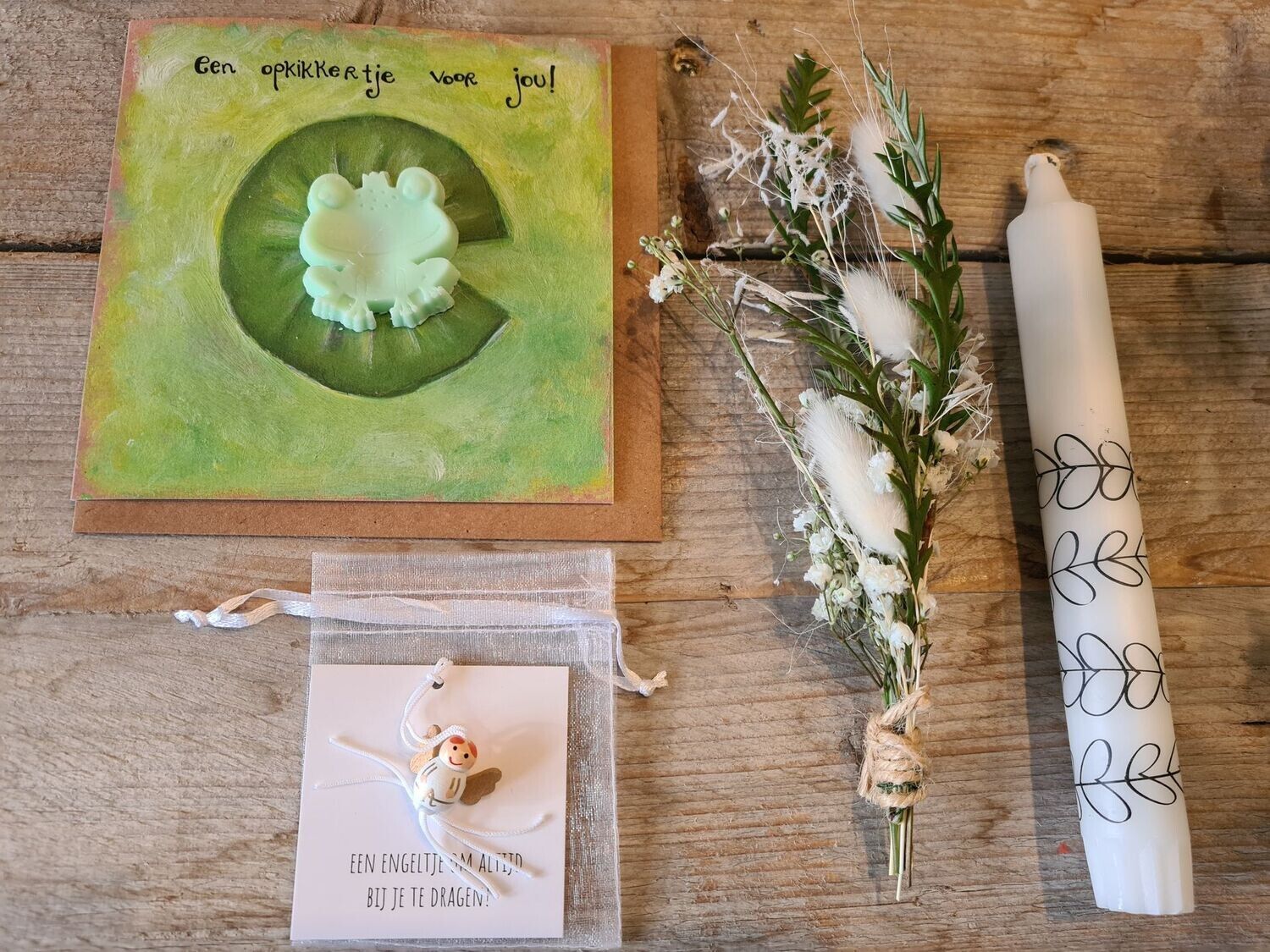 Doos met een wenskaart, een kaars en bloemen. Op de kaart staat een kikker op een waterlelie afgebeeld.